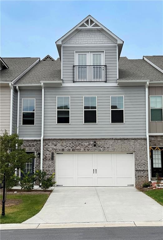 View of front of house with concrete driveway, brick siding, a shingled roof, a balcony, and an attached garage