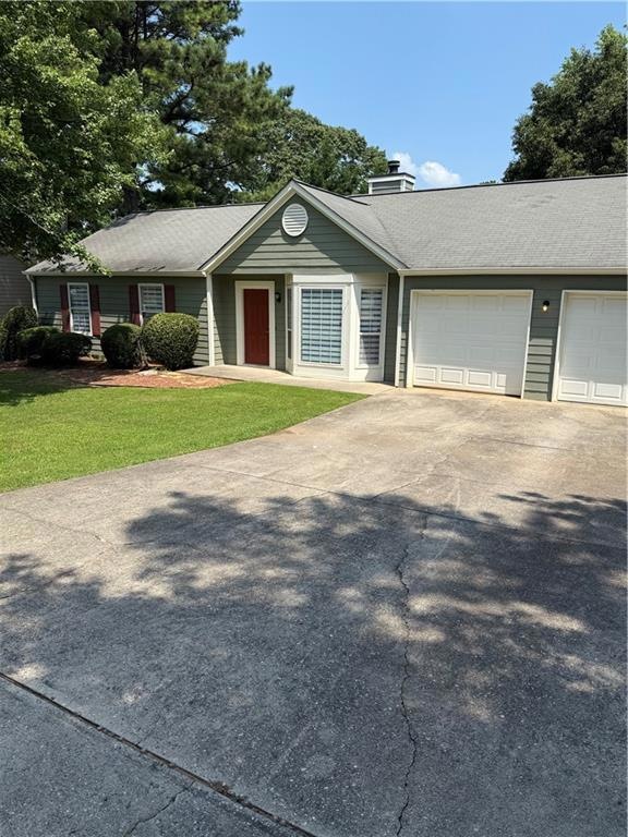 Ranch-style house featuring a front yard, driveway, a chimney, and an attached garage