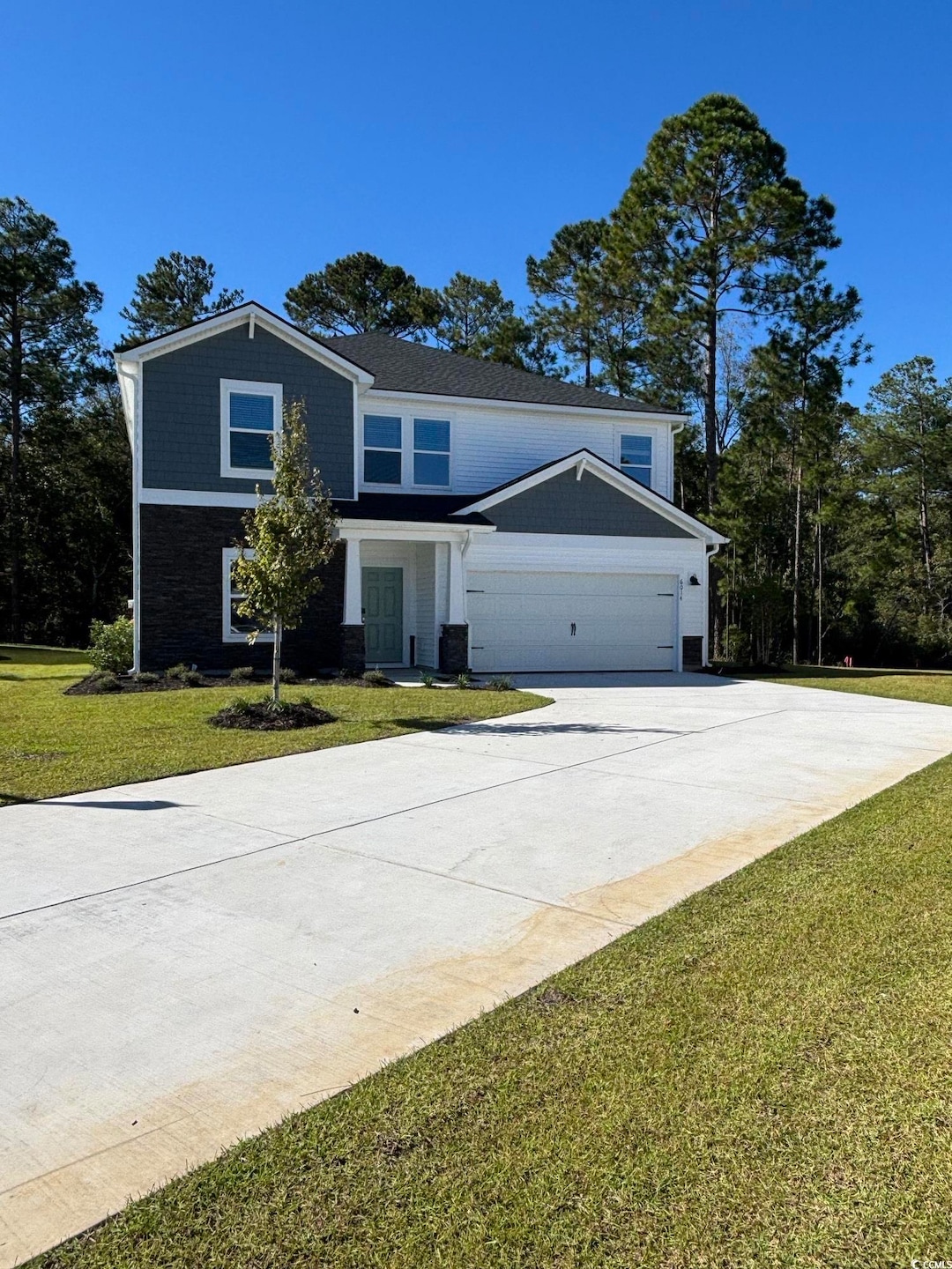 View of front of property featuring a front lawn, concrete driveway, stone siding, and an attached garage