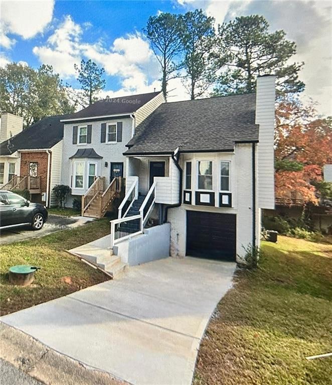 View of front of property with stairway, an attached garage, driveway, a front yard, and a chimney