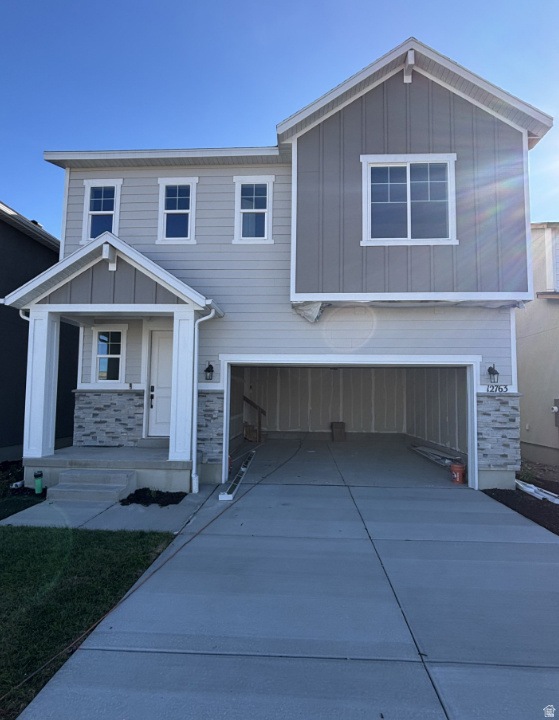 View of front facade featuring board and batten siding, a garage, driveway, and stone siding