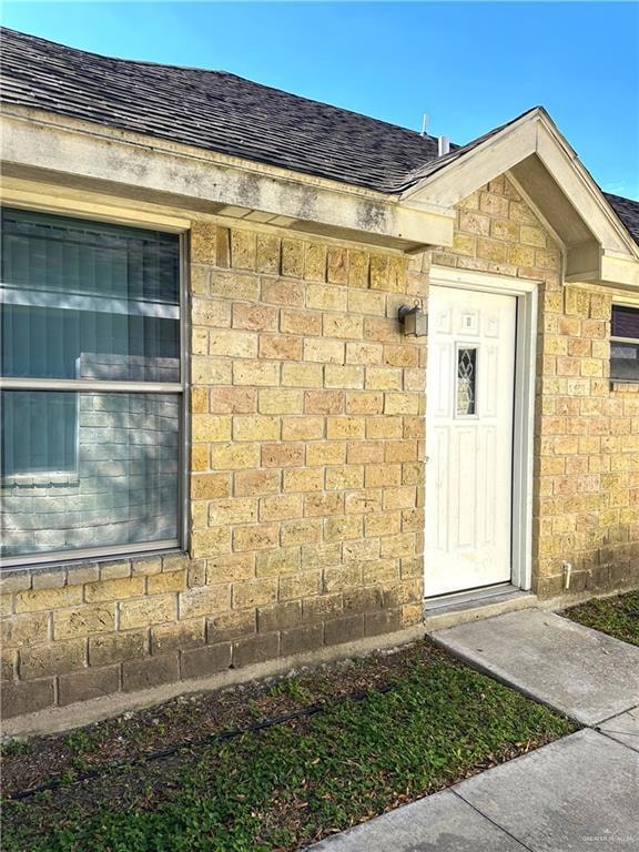 View of exterior entry featuring a shingled roof