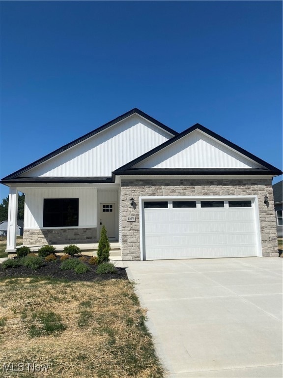 View of front of home featuring stone siding, a garage, driveway, and a porch