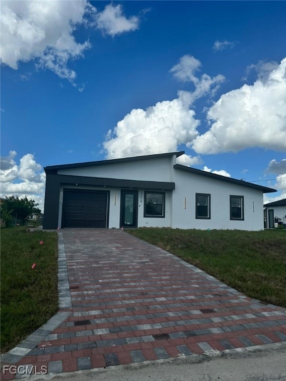 View of front facade featuring stucco siding, an attached garage, decorative driveway, and a front yard