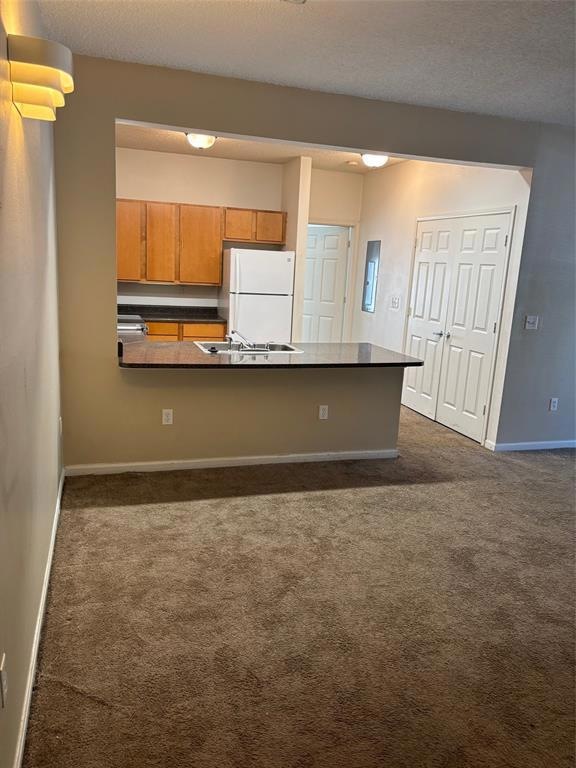 Kitchen with fridge, dark carpet, dark countertops, brown cabinetry, and a peninsula