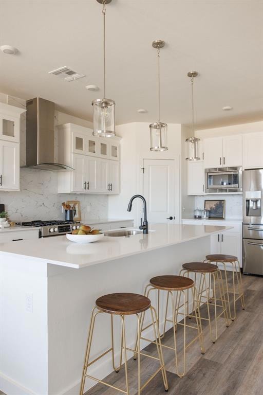 Kitchen with white cabinetry, wall chimney range hood, decorative light fixtures, backsplash, and stainless steel appliances
