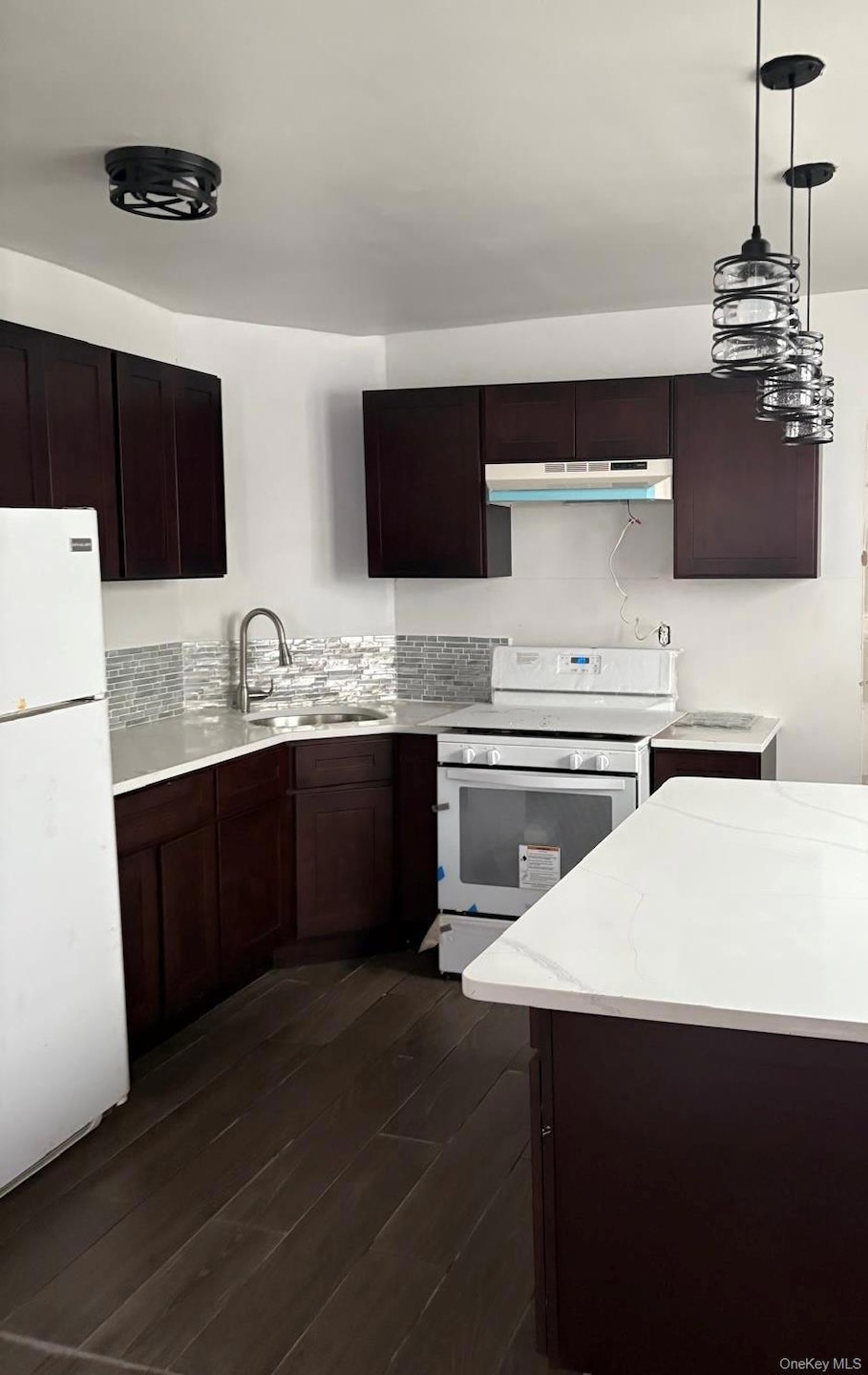 Kitchen featuring white appliances, dark brown cabinets, pendant lighting, and dark wood-type flooring