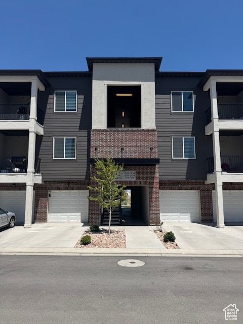 View of front of property with brick siding, a balcony, driveway, and an attached garage