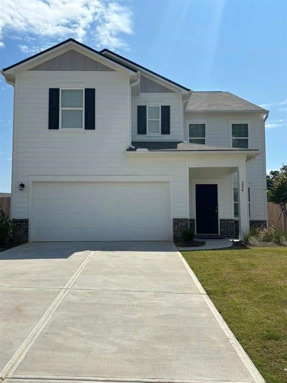 View of front of home with board and batten siding, an attached garage, driveway, a front lawn, and stone siding