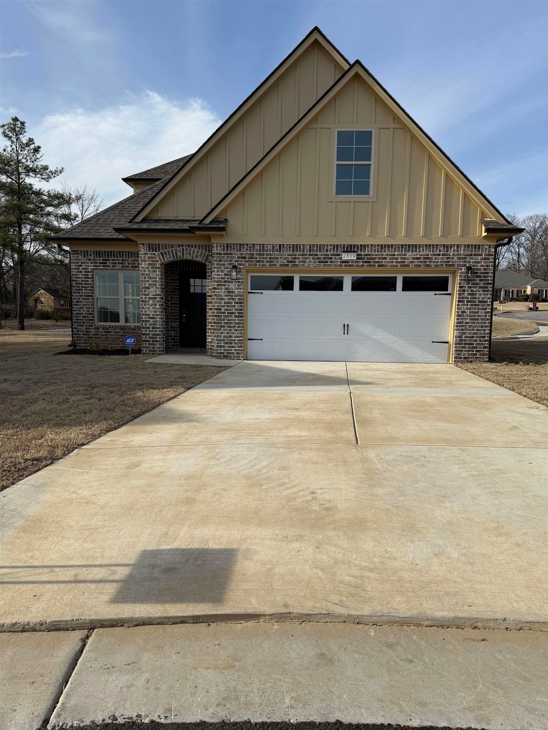 View of front facade with brick siding, board and batten siding, concrete driveway, and roof with shingles