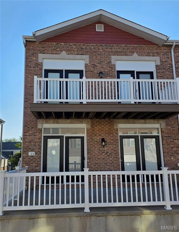 Back of house with brick siding and a balcony