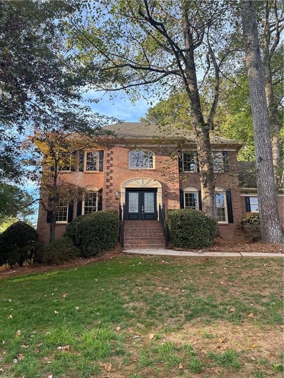 View of front of house featuring a front lawn, brick siding, and french doors