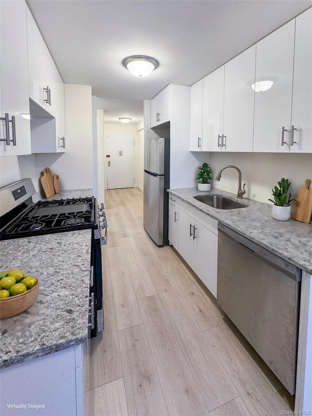 Kitchen with stainless steel appliances, light wood-type flooring, white cabinets, light stone countertops, and modern cabinets