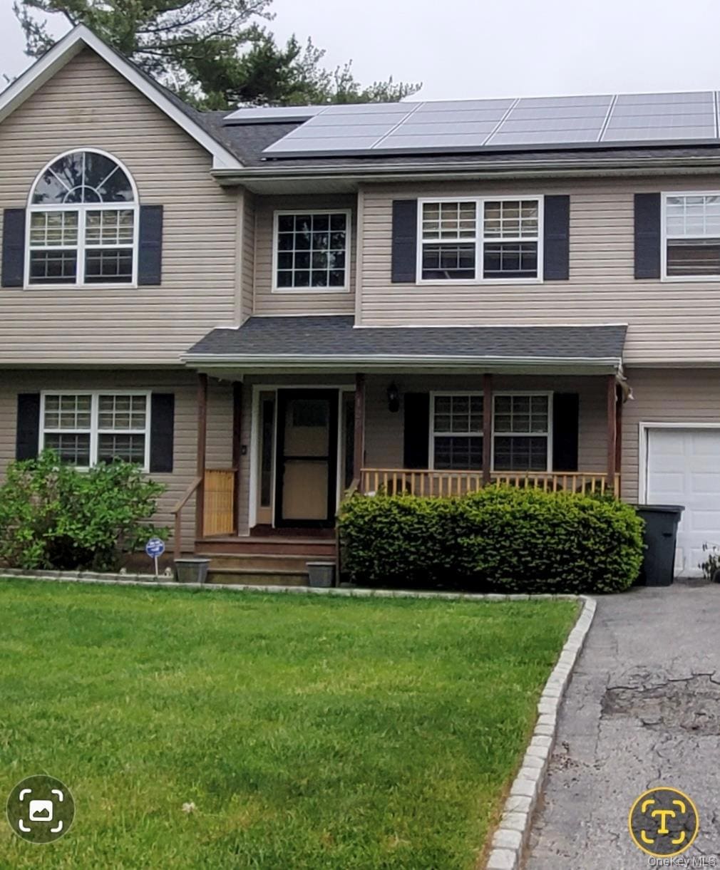 View of front of property with a porch, a front lawn, roof mounted solar panels, and driveway