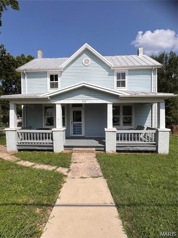 View of front of house featuring a chimney, a porch, and a front yard