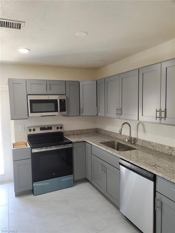 Kitchen featuring appliances with stainless steel finishes, gray cabinetry, light stone countertops, and a textured ceiling