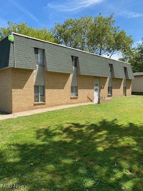 Rear view of property with mansard roof, brick siding, and a yard