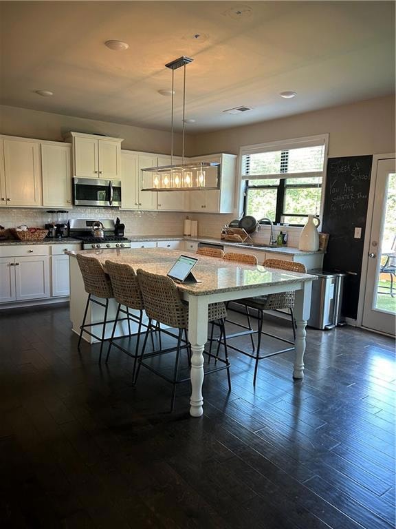 Kitchen featuring white cabinets, decorative light fixtures, stove, light stone countertops, and dark wood finished floors
