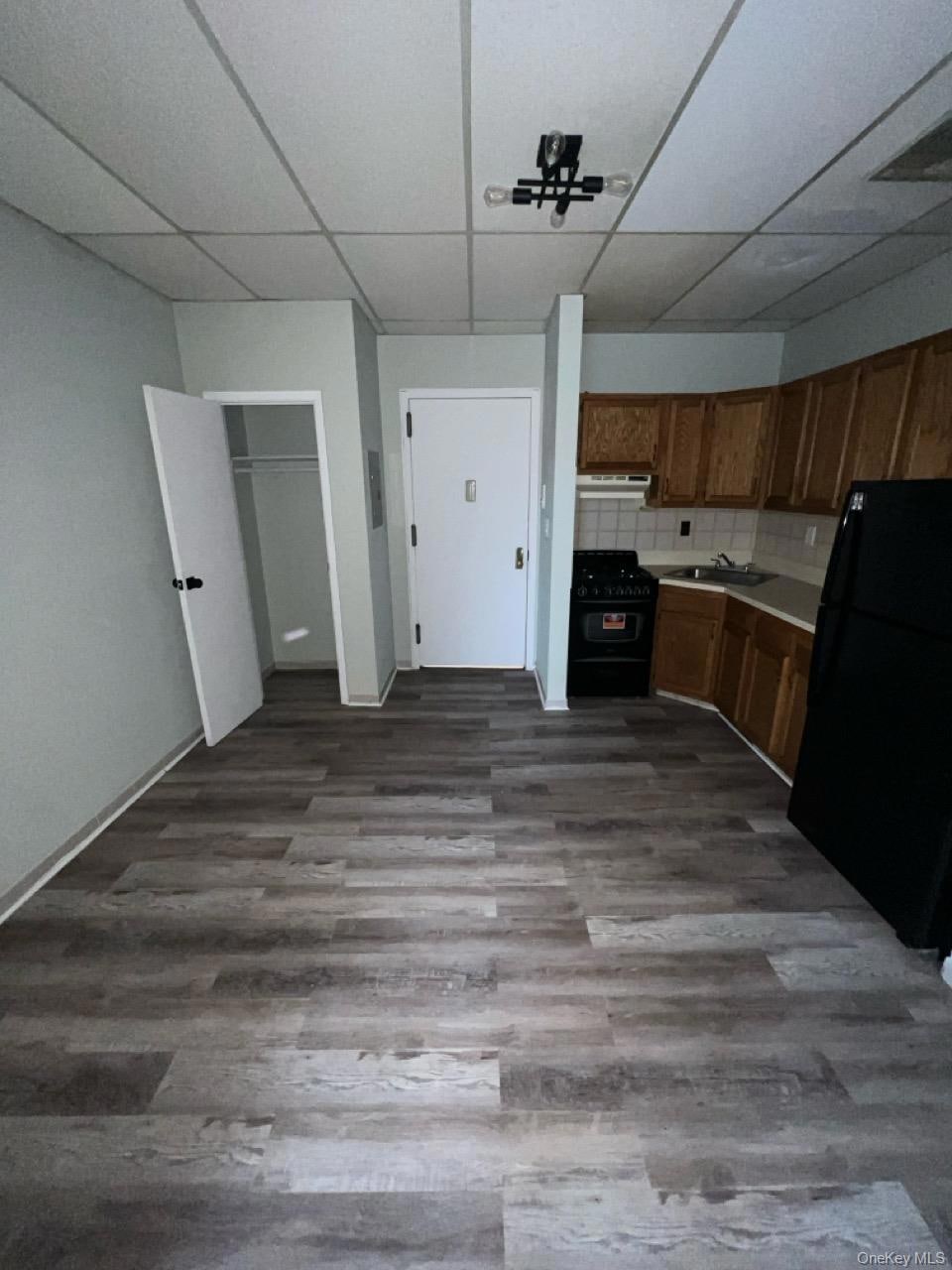 Kitchen featuring light countertops, tasteful backsplash, a paneled ceiling, black appliances, and dark wood-style flooring