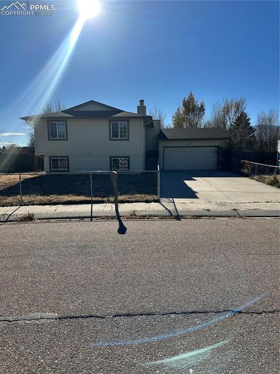 View of front of property featuring a fenced front yard, concrete driveway, an attached garage, and a chimney