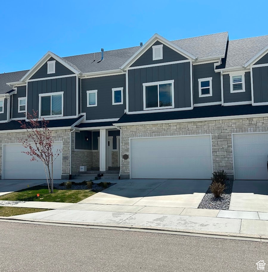 Craftsman-style home featuring stone siding, board and batten siding, driveway, an attached garage, and covered porch