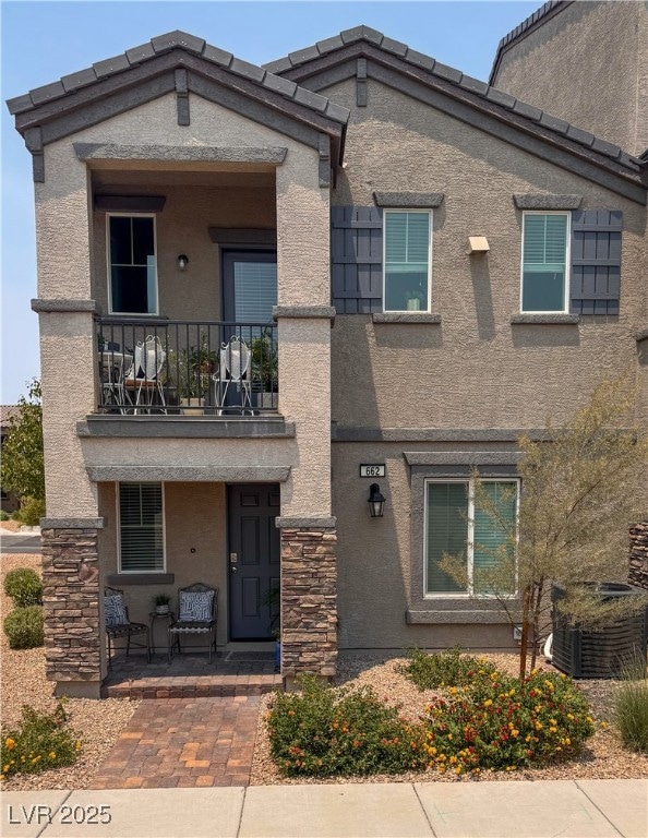 View of front of house with a balcony, stucco siding, a porch, and stone siding