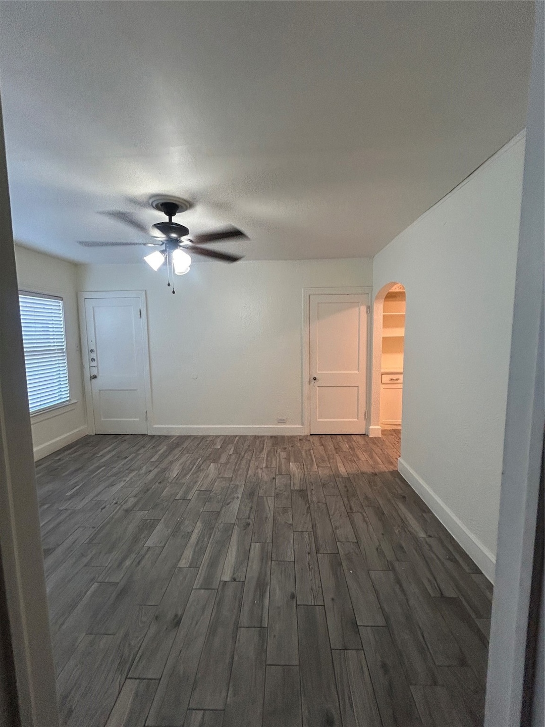 Spare room featuring arched walkways, dark wood-style floors, and a ceiling fan