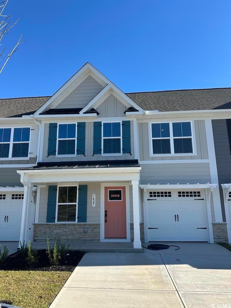 View of front of home with covered porch, stone siding, a garage, and driveway
