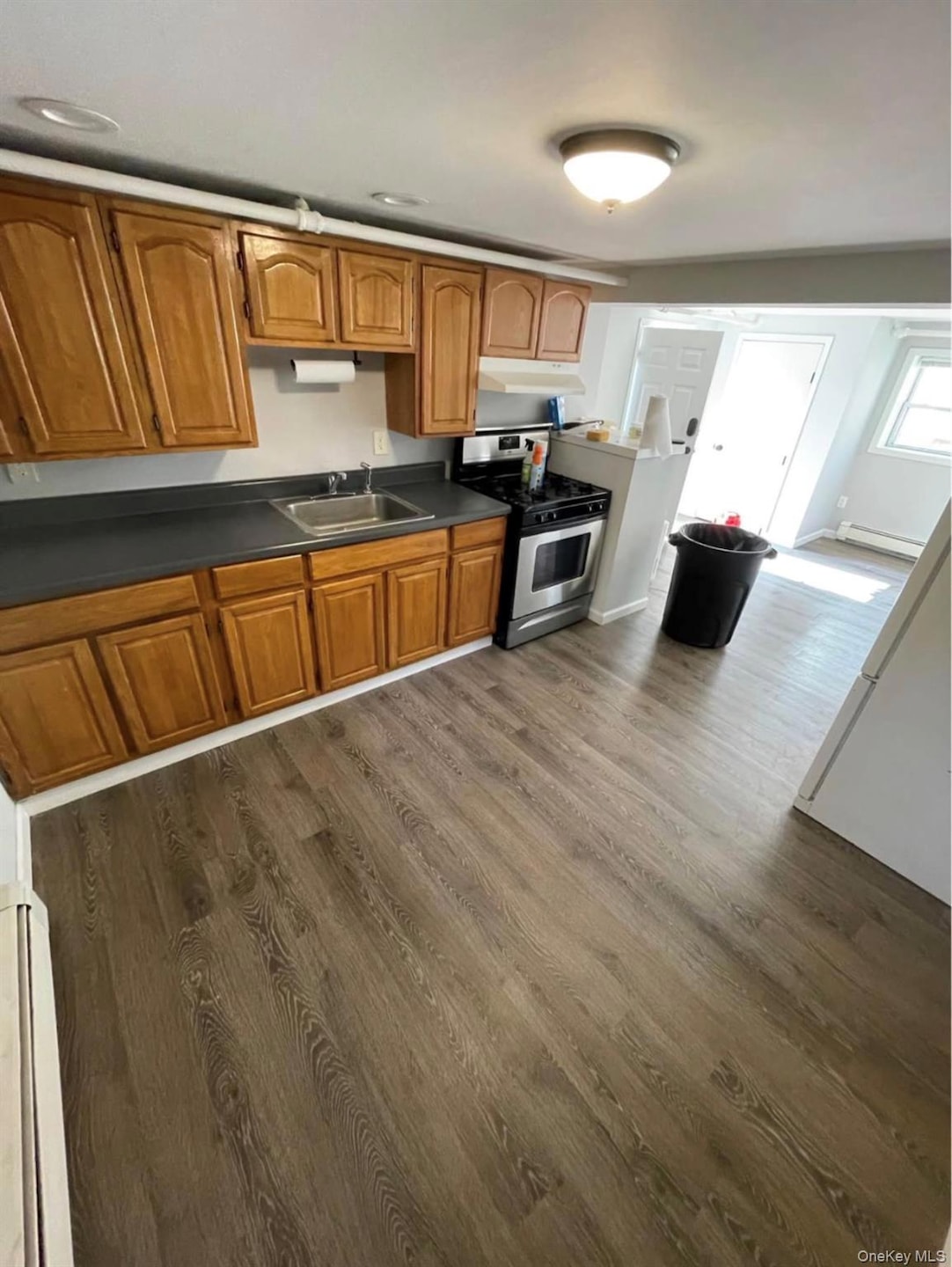 Kitchen with dark countertops, gas range, dark wood finished floors, brown cabinetry, and baseboard heating
