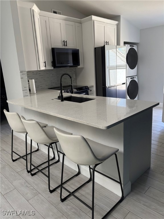 Kitchen with a breakfast bar, freestanding refrigerator, black microwave, wood finish floors, and vaulted ceiling
