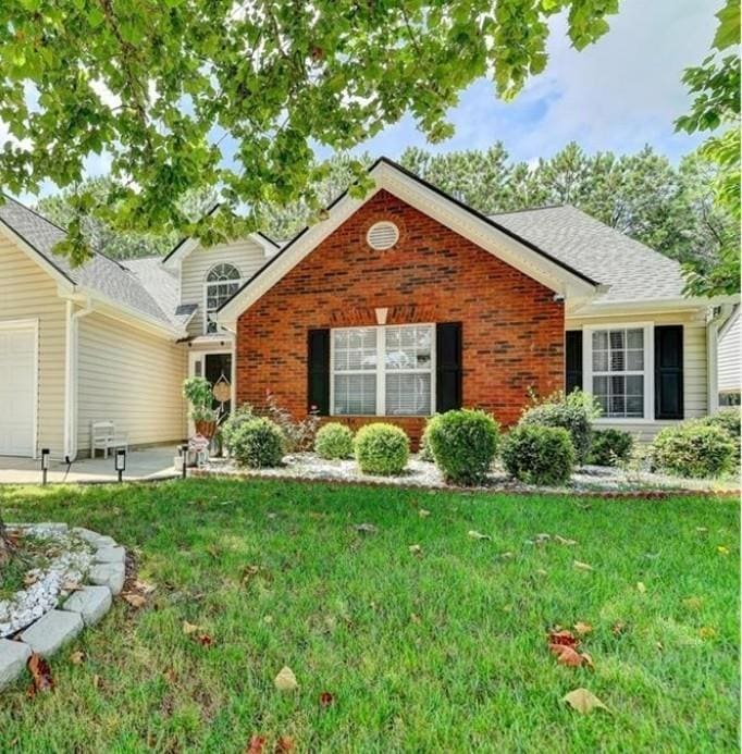 View of front of house featuring brick siding, a front yard, an attached garage, and roof with shingles