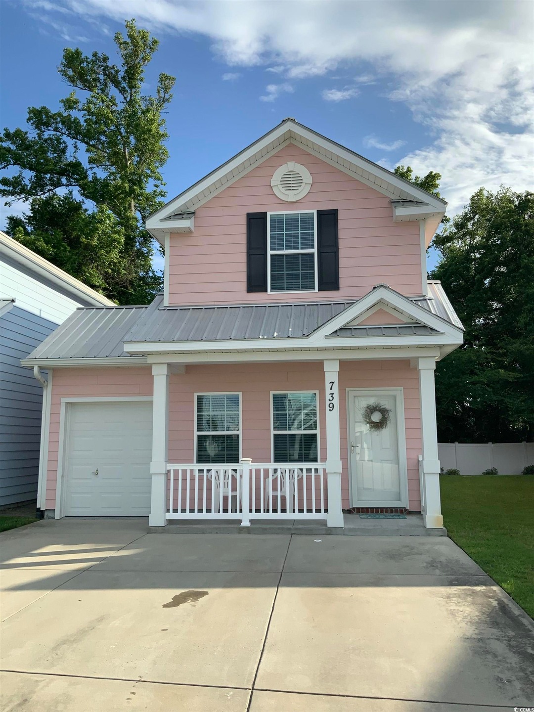 View of front of property featuring covered porch, driveway, metal roof, a garage, and fence