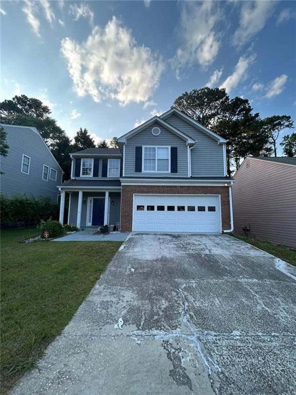 Traditional-style home featuring brick siding, a porch, concrete driveway, an attached garage, and a front lawn