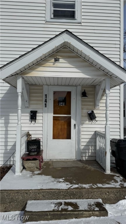 Snow covered property entrance featuring a porch