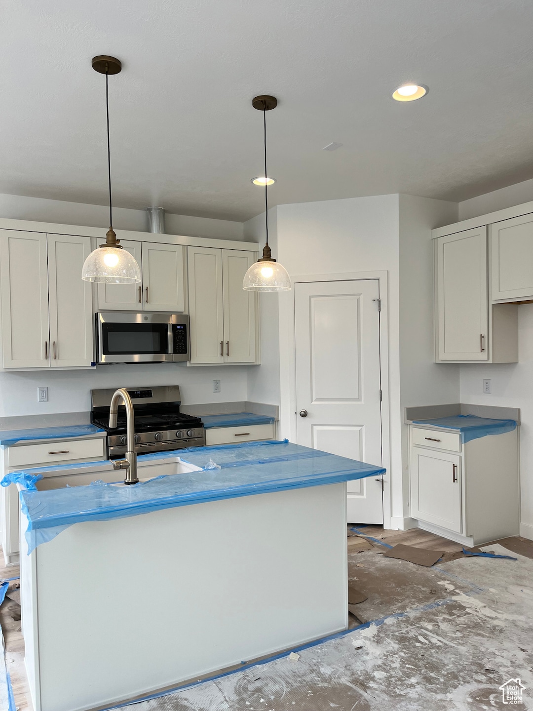 Kitchen with appliances with stainless steel finishes, a kitchen island with sink, white cabinetry, hanging light fixtures, and recessed lighting