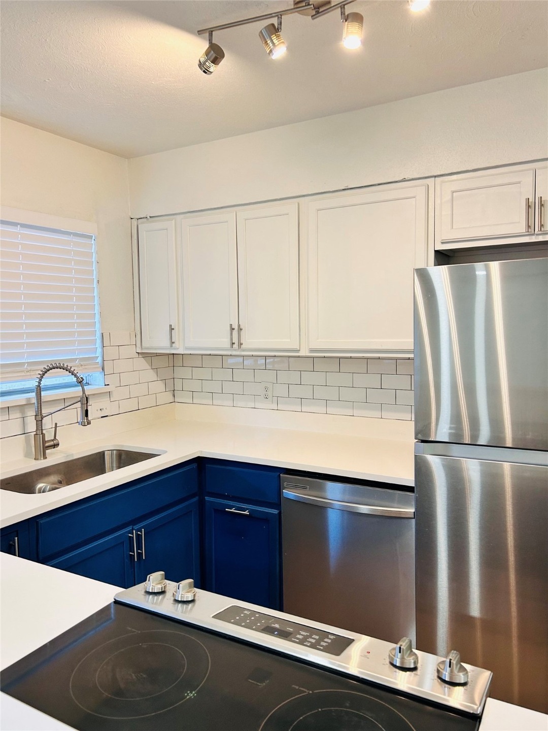 Kitchen featuring appliances with stainless steel finishes, tasteful backsplash, white cabinetry, blue cabinetry, and light stone countertops