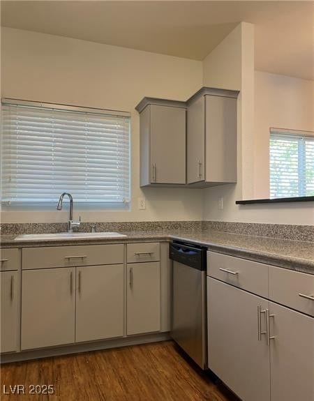 Kitchen featuring dark wood-style floors, stainless steel dishwasher, dark countertops, and gray cabinets