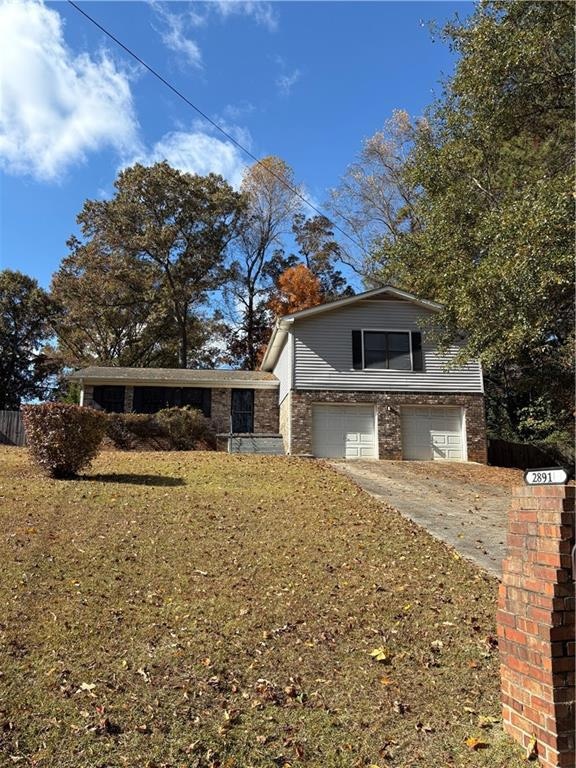 View of front of house featuring an attached garage, concrete driveway, brick siding, and a front yard