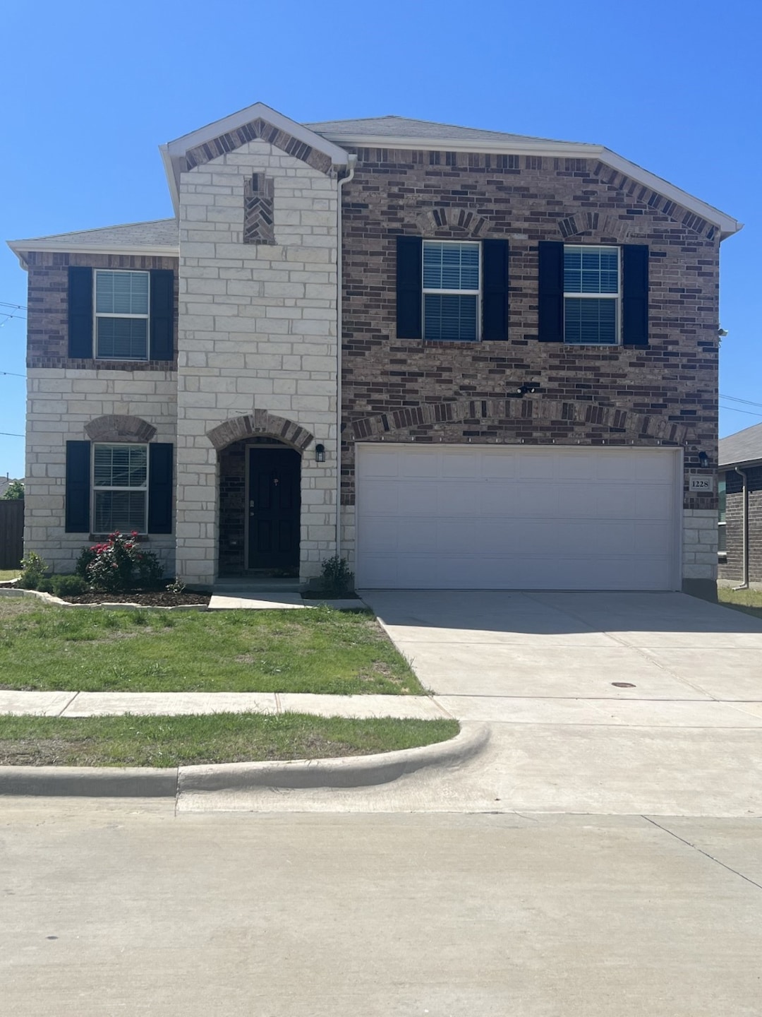 View of front of house featuring a garage, driveway, brick siding, stone siding, and a front yard