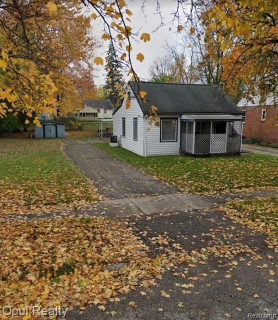 View of front of home featuring asphalt driveway, a shed, and a front yard