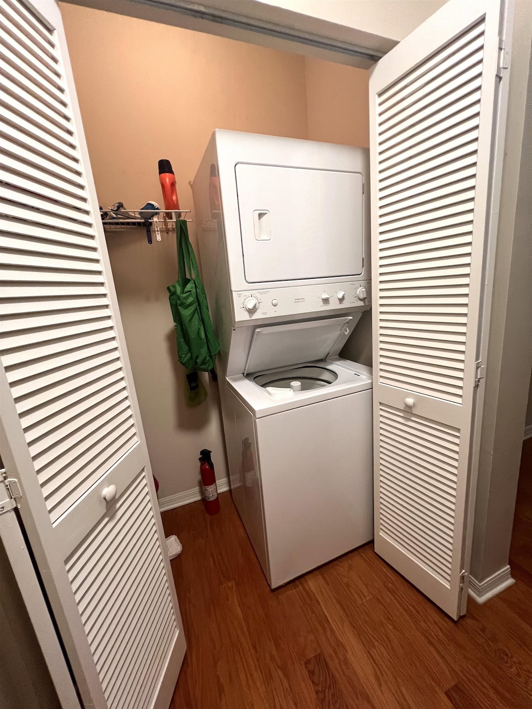 Washroom with dark wood-style flooring and stacked washing machine and dryer