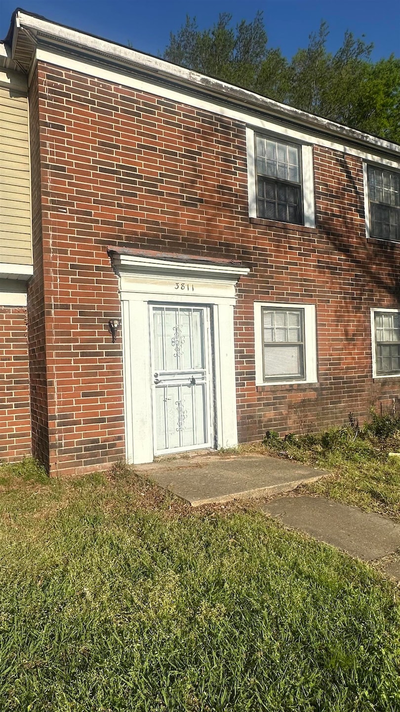 Entrance to property with a lawn and brick siding