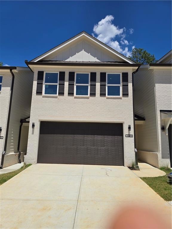 View of front of property featuring board and batten siding, concrete driveway, an attached garage, and brick siding