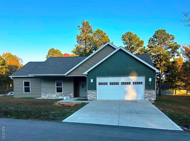 View of front of property with stone siding, a front yard, concrete driveway, covered porch, and board and batten siding