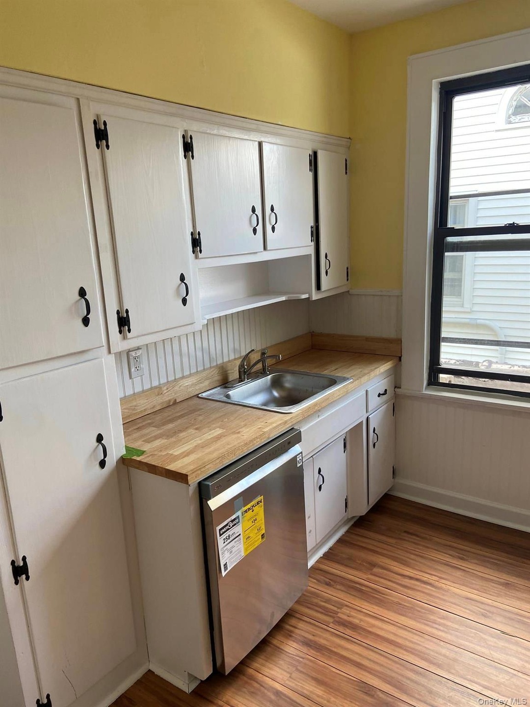 Kitchen with white cabinets, stainless steel dishwasher, dark wood-style floors, wainscoting, and butcher block counters