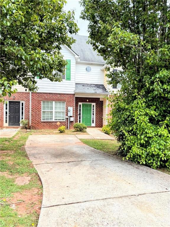 View of property featuring driveway and brick sidi