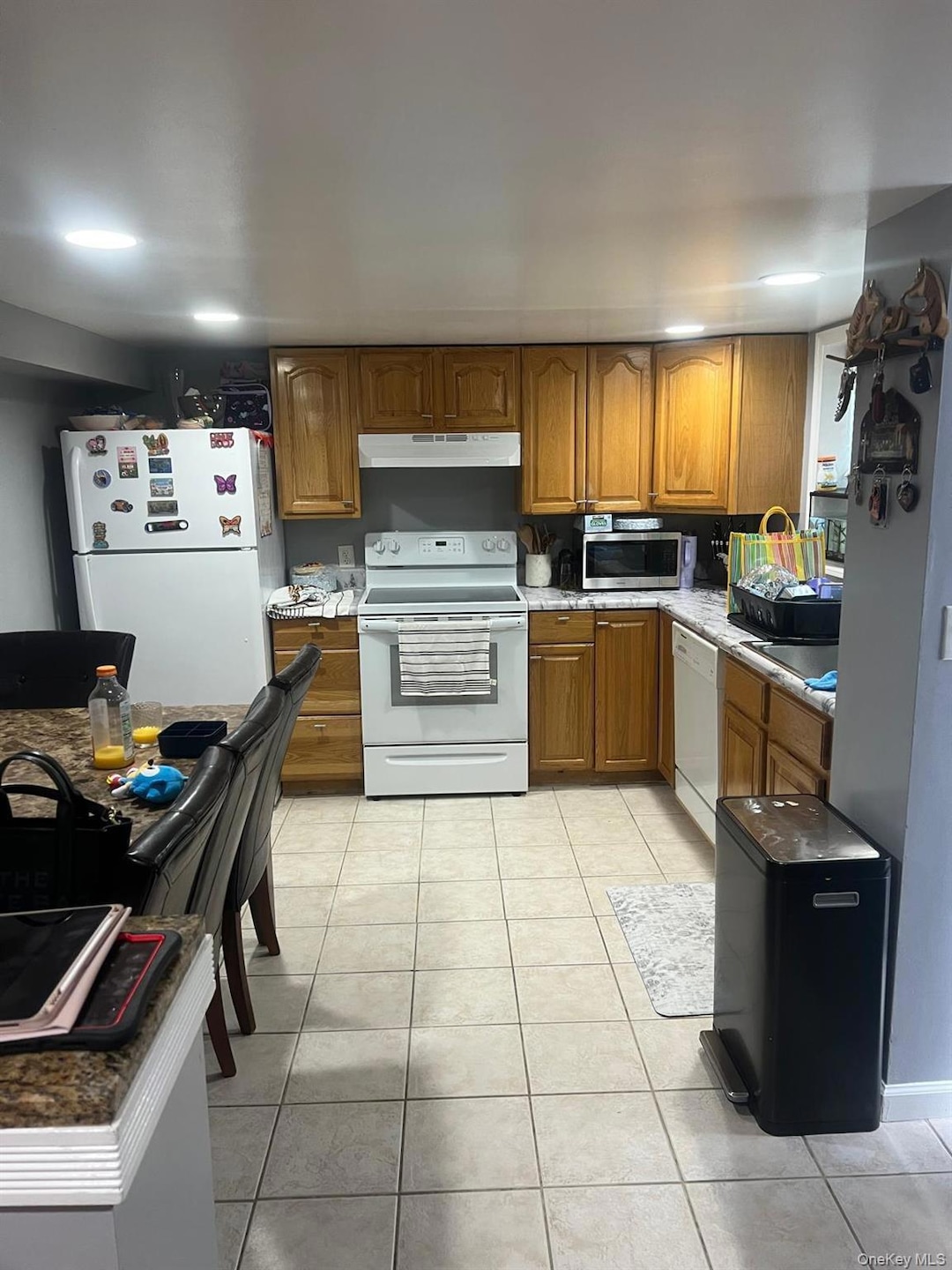Kitchen with brown cabinets, appliances with stainless steel finishes, light tile patterned floors, and under cabinet range hood