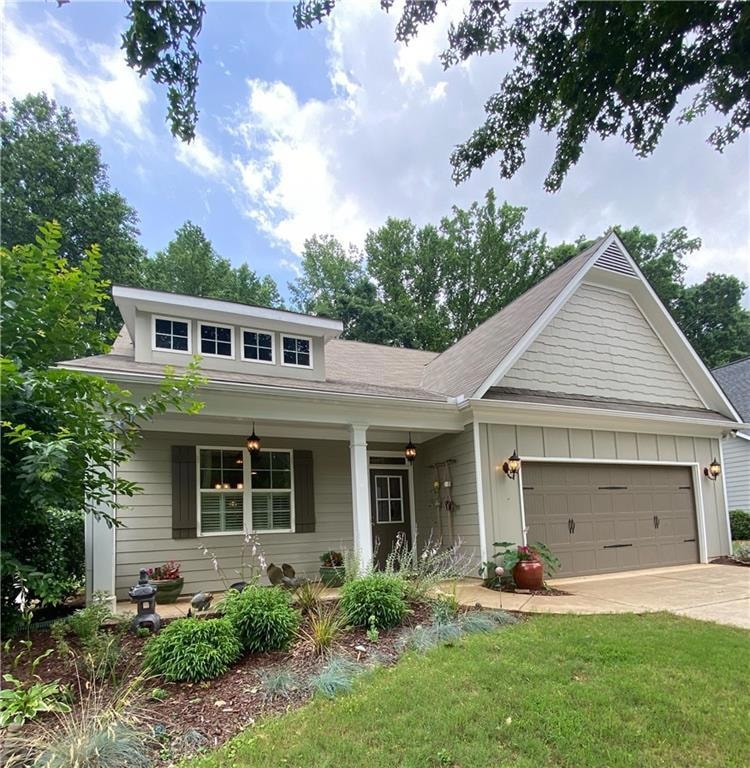 View of front of house with covered porch, driveway, an attached garage, board and batten siding, and a front lawn