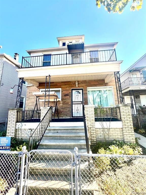 View of front facade with a gate, a fenced front yard, brick siding, and a balcony