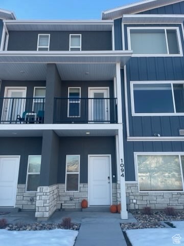 View of front of property with stone siding, board and batten siding, a balcony, and a porch